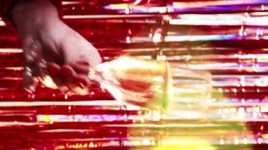Dikey video. Noel partisi. Tatil neşesi. Tanımlanamayan bir kadın bir bardak şampanya ile dans ediyor. Renkli bokeh ışığı ve parlak kırmızı süs arkaplan..