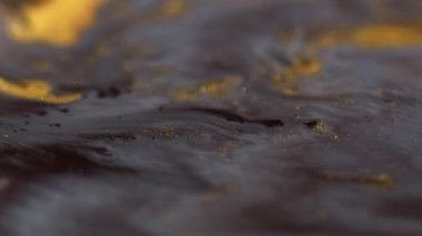 Boya sızıntısı. Parıldayan sıvı dökülmüş. Odaklanmamış siyah altın sarısı beyaz renk ışıl ışıl desen sıvı akış hareketi soyut sanat arka planı.