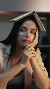 Dikey video. Yorgun öğrenci. Geç saatlere kadar çalışıyorum. Kafasında kitapla çok çalışan yorgun bir kadın masamda uyuyor ve geceleri laptopta yazı yazıyor..