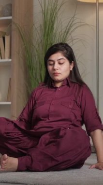 Dikey video. Evde yoga. Esneklik Asana. Sağlıklı rahatlık. Nilüfer pozisyonunda rahat genç bir kadın oturma odasında ustrasana deve pozu egzersizi yapıyor..