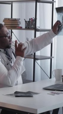 Dikey video. Teşhis konsültasyonu. Klinik sağlık hizmeti. Hasta randevusu. Modern hastane toplantısındaki kadına hastalığı açıklayan röntgen incelemesi yapan profesyonel bir doktor..