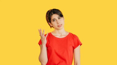 Kafası karışmış kırmızı elbiseli kadın belirsiz görünüyor sarı boş alan arka planında izole edilmiş şüphe duygularını ifade ediyor..