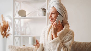 Spa sohbeti. Dostça bir ilham. Beyaz banyo spa havlusu ve duştan sonra telefonda konuşan enerjik gülen genç kız..