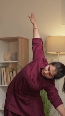 Dikey video. Ev içi yoga. Aktif yaşam tarzı. Bedensel zihin sağlığı. Neşeli kadın oturma odasında esneklik egzersizi yapıyor..