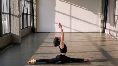 Jimnastik egzersizi. Ayrılma egzersizi. Egzersiz yoga yapan sağlıklı bir kadın güneş ışınları jimnastik salonundaki spor minderinde asana kas esneme egzersizi yapıyor..