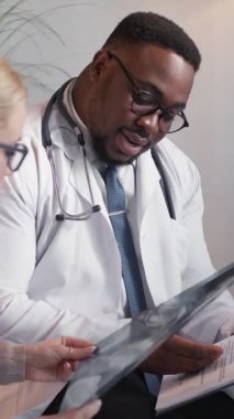 Dikey video. Doktorlar işbirliği yapıyor. Tıbbi tartışma. Profesyonel zeki adam doktor, teşhis raporunu röntgen taramasıyla ve kadın doktorla birlikte kontrol ediyor..