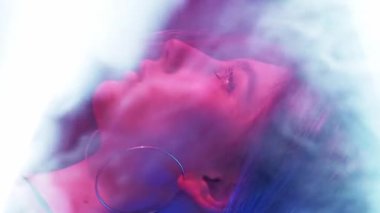 Dikey video. Neon ışıklı surat. Siber punk güzeli. Disko 80 'lerin gece hayatı. Pembe mavi renkli parlak profil. Koyu renkli beyaz duman bulutu içinde bir kız..