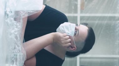 Dikey video. Salgın izolasyonu. Ofis kilitlendi. Sıkıcı, yorgun, kilolu, tıbbi maskeli, korunaklı plastik çalışma alanında çalışan,.