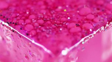 Parlak sıvı damlası. Parlak sıvı doku. Odaklanmamış pembe renkli ışıltılı pullu parçacıklar boya damlaları yüzen döküntü cam küp kenar soyut sanat arka planı.