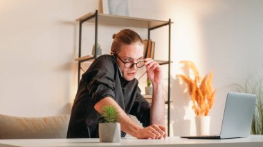 İş teknolojisi. İş uzmanıyım. Siyah gömlekli başarılı genç adam, elinde gözlük tutarken akıllı telefon kullanıyor. Bilgisayarda bilgisayarını çalıştırmadan önce..