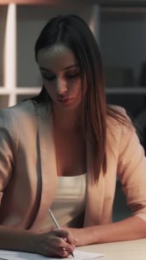 Dikey video. Ev ödevi. Çevrimiçi öğrenme. İş yerindeki sakin iş kadını el yazısı notları ve dizüstü bilgisayar sınavı hazırlığı.