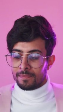 Dikey video. Zafer partisi. Kazanan neşe. Başarı kutlaması. Mor renkli, neon ışıklı, mutlu, gözlüklü, gururlu adam pembe üzerinde dans etmekten zevk alıyor..