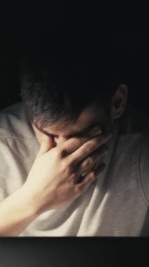 Dikey video. İş yoğunlaşması. Fazla mesai. Gece devriyesi. Stresli çalışkan iş adamı dizüstü bilgisayarda yazı yazıyor gözlerini ovuşturuyor karanlık odada çay içiyor..