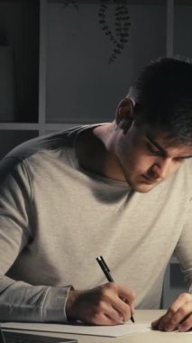 Dikey video. Gece çalışması. Sınav hazırlığı. Online eğitim. Yoğunlaştırılmış özenli öğrenci notlar alıyor. Geç saatlerde karanlık evde dizüstü bilgisayar kullanarak ders çalışıyor..