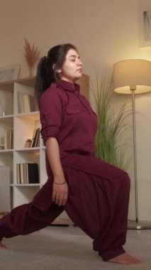 Dikey video. Esneme egzersizi. Ev antrenmanı. Sağlıklı bir yaşam tarzı. Genç sportif kadın, virabhadrasana savaşçısı ayaklarına poz veriyor..