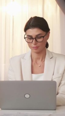 Dikey video. Başarılı bir iş. Yorgun bir kadın. Projeyi bitir. Çalışkan bayan bilgisayarını kapatıyor. Gözlüklerini çıkarıyor. Köprünün iç tarafına dokunuyor..