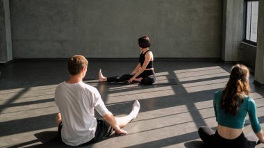 Jimnastik dersi. Yoga egzersizi. Spor eğitmeni kadın spor eğitmeni. Spor salonundaki spor salonundaki paspasın üzerinde vücut esnetme egzersizi yapan insanlar..