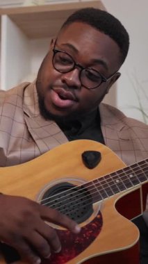 Dikey video. Müzik öğretmeni. Gitar dersi. Takım elbise giymiş mutlu dost canlısı uzman bir eğitimci sanat okulunda kapalı alanda şarkı akorlarını açıklıyor..