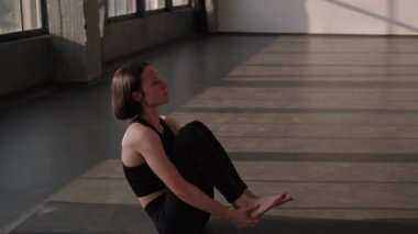 Jimnastik pratiği. Pilates egzersizi. Spor kıyafetli sağlıklı bir kadın spor salonunda spor salonundaki yoga minderinde ayak tutarak bacak kaldırma egzersizi yapıyor..