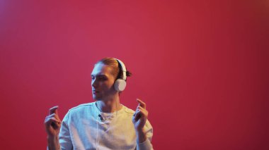 Kulaklık kullanıyor. Müzik dansı. Kırmızı stüdyo arka planında izole edilmiş kulaklıkları olan pozitif yaratıcı genç adam şarkı dinliyor..