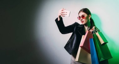 Alışveriş selfie 'si. Kara Cuma. Alışverişkolik yaşam tarzı. Gözlüklü göz kamaştırıcı kadın telefon kamerasında boş bir alanda poz veriyor..