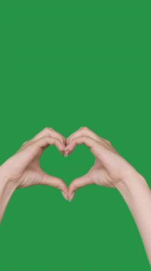 Dikey video. Kalp hareketi. Aşk işareti. Sevgi ve hayranlık. Yeşil renkli anahtar boş arkaplanda romantik bir sembol gösteren kadın elleri.