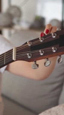 Dikey video. Akort aleti. İlham verici bir kadın. En sevdiğim hobi. Aydınlık odanın içinde akustik gitar sesi ayarlayan tanınmamış bir kadın..