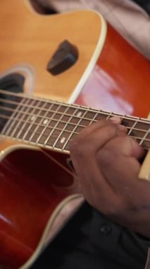 Dikey video. Gitar çalıyor. Şarkı performansı. Blues müziği. Yetenekli erkek sanatçının elleri Capo ile akustik telli enstrüman üzerinde caz akorları çalışıyor..