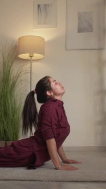 Dikey video. Yoga eğitimi. Evde spor salonu. Sağlıklı bir hobi. Sakin esnek kadın Bhujangasana kobrası oturma odasında uttana shishosana pozu veriyor..