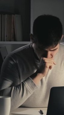 Dikey video. Yorucu bir iş. İnternet kariyeri. Fazla mesai hayatı. Uykucu, çalışkan, serbest çalışan, kahve içen, karanlık ev ofisinde dizüstü bilgisayar kullanan bir adam..
