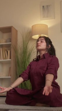Dikey video. Yoga devrede. Meditasyon eğitmeni. Ruhsal rahatlık. Lotus 'ta kadın koç poz veriyor. Oturma odasındaki internet kursunda Mudra jesti öğretiyor..