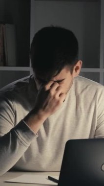 Dikey video. Fazla mesai. Son teslim tarihi stresi. İş yorgunluğu. Uykucu, yorgun, serbest çalışan, dizüstü bilgisayarda yazan, işini bitiren, gözlerini ovuşturan, karanlık ofis odasında uyuyan bir erkek..