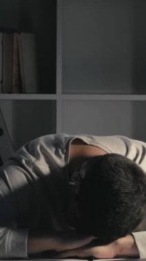 Dikey video. Eğitim yorgunluğu. Akademik yorgunluk. Masa uykusu. Gece geç saatlere kadar ders çalıştıktan sonra masa başında uyuyan yorgun erkek öğrenci..