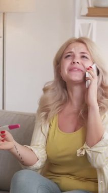 Dikey video. Harika haberlerim var. Heyecanlı kadın. Mutlu hamilelikler. Elinde pozitif bir test sonucu tutan ilham verici bir bayan akıllı telefondan konuşuyor koltuğun içinde oturmaktan keyif alıyor..