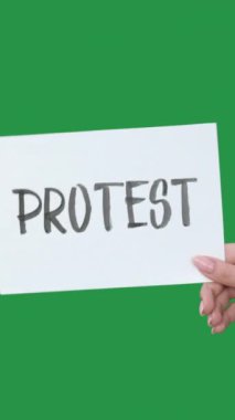 Dikey video. Protesto işareti. Vuruş levhası. Yeşil renkli anahtar boş arkaplan üzerinde izole edilmiş harf metnini gösteren kadın eli.