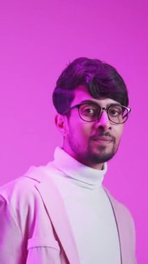 Dikey video. Romantik bir jest. Sevgililer Günü selamı. Aşk flörtü. Mor renkli, neon ışıklı, kendine güveni tam, gözlüklü yakışıklı adam pembe üzerine izole bir şekilde hava öpücüğü üflüyor..