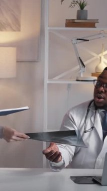 Dikey video. Doktor ekip çalışması. Radyoloji teşhisi. Profesyonel sağlık hizmeti. Dizüstü bilgisayardaki erkek doktor klinikteki üniformalı kadın hemşireyle röntgen taramasını onaylıyor..