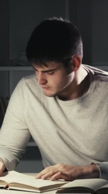 Dikey video. Uyumaya çalış. Son teslim tarihi yorgunluğu. Gece okumaları. Yorgun erkek öğrenci kitap yaprakları ovuyor gözlerini ovuşturuyor esniyor karanlık evde geç saatlere kadar masa başında kestiriyor..