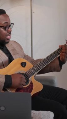 Dikey video. Müzisyen blogu. Gitar çevrimiçi kursu. Akort dersi. Profesyonel erkek, evdeki internet dizüstü bilgisayar dersinde oyun dersi veriyor..