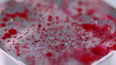 Mürekkep damlası. Parlak sıvı dokusu. Bulanık, kırmızı, parlak, pullu, şeffaf, sıvı, boya damlaları. Bokeh ışıklarıyla hareketli, soyut sanat arkaplanı..