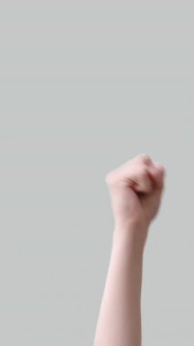 Dikey video. Zafer kutlaması. Zafer sevinci. Kazanan kadın el sıkışması sıkılmış yumruğunu kaldırarak V işaretini göstermiş. Işık nötr arka planda izole edilmiş..