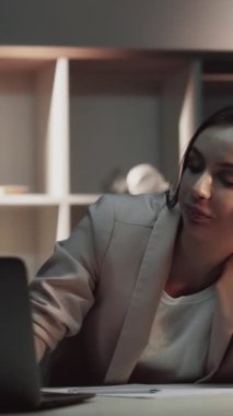 Dikey video. Uykucu işçi. Aşırı çalışma yorgunluğu. Uzun çalışma saatlerinden sonra bilgisayarını kapatmak için esnemekten yorgun düşmüş bir kadın geç kaldı..