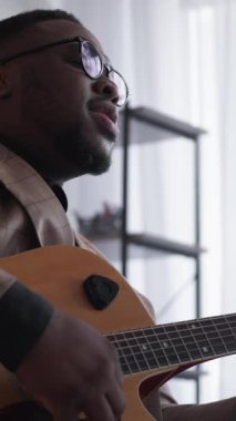 Dikey video. Gitar söylüyor. Müzik sanatçısı. Vokalist. Yetenekli yaratıcı adam evde akustik telli enstrüman ile blues çalıyor..