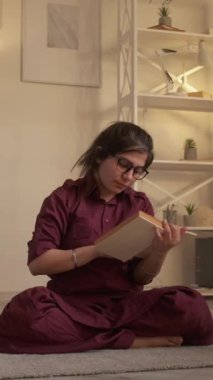 Dikey video. Yoga kitabı. Boş vakitleri değerlendiriyorum. Sıcak bir hafta sonu. Hayalperest barışçıl kadın evde, oturma odasında dinlenirken ilginç meditasyon edebiyatının keyfini çıkarıyor..