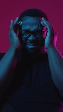 Dikey video. Baş ağrısı. Stres sorunu. Anksiyete sorunu. Burgonya arka planında izole edilmiş neon ışıkta migren ağrısı çeken üzgün bir adam..