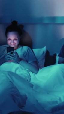 Dikey video. Yataktaki çift geceleri teknolojiyle meşgul. Telefoncu adam kullanıyor. Bilgisayarda çalışıyor, modern yaşam tarzını benimsiyor..