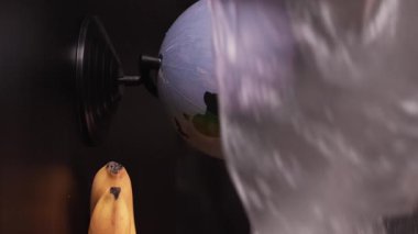 Dikey video. Plastik kirliliği. Doğa koruma. Ekoloji koruması. Dünyayı kaplayan polietilen film koyu renkli taze organik meyve kompozisyonu ile.