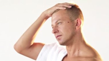 Erkek tazeliği. Sabah rutini. Üstsüz, sarışın, atletik vücut havlusuyla çıplak omuzunda kısa saçlara dokunan beyaz boşlukta izole edilmiş bir adam..