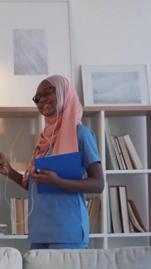 Dikey video. Doktor molası. Müzik dinliyor. Gadget 'ın boş vakti. Modern klinikteki kulaklıklarda şarkı listesinin keyfini çıkaran üniformalı neşeli hemşire..