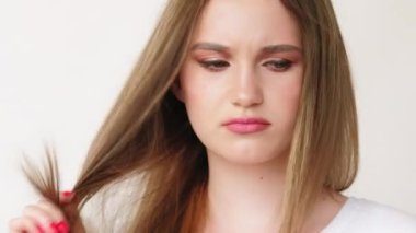 Saç problemi. Vitamin terapisi. Maske şampuanı. Beyaz tişörtlü hayal kırıklığına uğramış kadın arka planda izole edilmiş hasarlı kötü sonlara bakıyor..